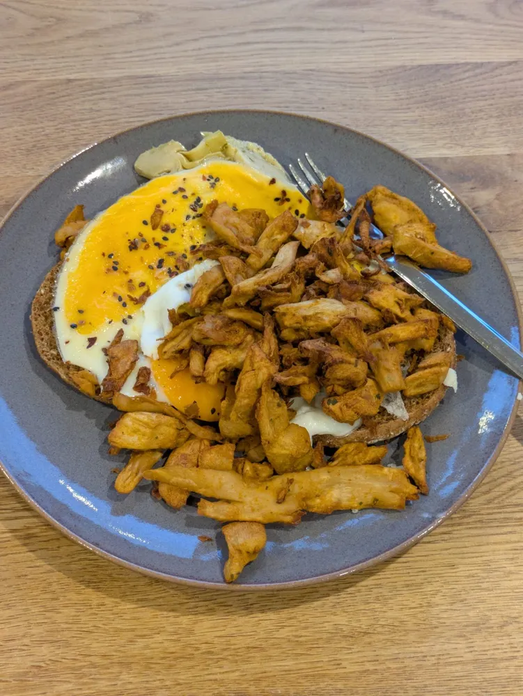Toast with fried egg, plant-based chicken pieces and artichokes.